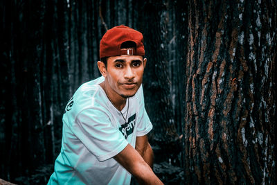 Portrait of young man standing against tree trunk