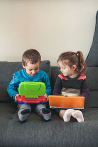 Boy and girl playing with toy laptop while sitting on sofa