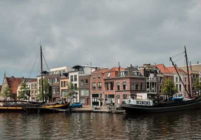 Sailboats moored on river by buildings against sky