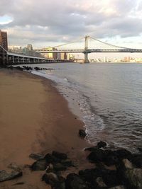 Suspension bridge over river against cloudy sky