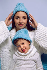 Mother and son in white sweaters and blue hats stand on a blue background in the studio