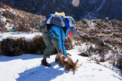 Young woman with  large backpack petting ginger dog on hike along the himalayan ridge in winter