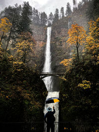 Blurred motion of person by waterfall in forest during autumn