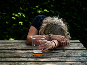 Woman having beer while sitting at table in yard