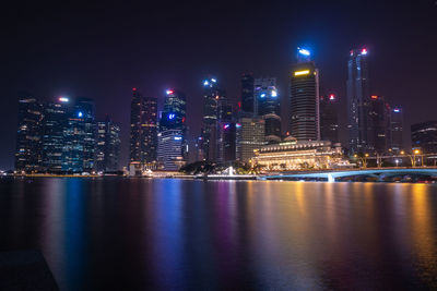 Illuminated city by river against sky at night