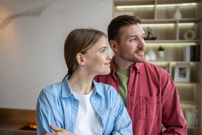 Happy family couple look at window together discussing something, daydreaming planning about future