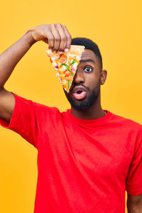 Portrait of young man holding heart shape against yellow background