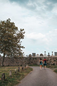 Rear view of people walking by trees against sky