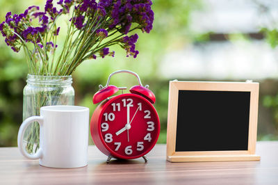 Close-up of alarm clock with coffee mug and blackboard on table at home