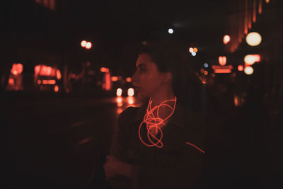 Young woman looking away while standing on road at night