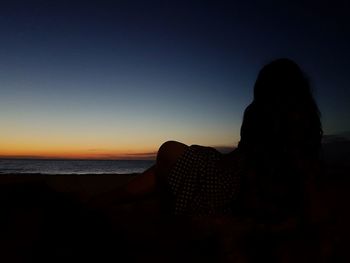 Rear view of silhouette woman sitting on beach at sunset