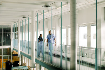 Male and female colleagues talking while walking in corridor at hospital