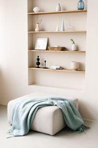 Light pouf next to blue plaid near shelves in the wall with decor. interior design of modern living