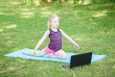 Cute girl exercising on field with laptop on grass