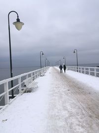 People on street by sea against sky during winter