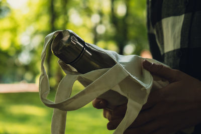 Close-up of unrecognizable female hand holding water bottle from eco bag. reusable steel thermo