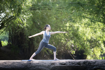 Full length of woman with arms raised against trees