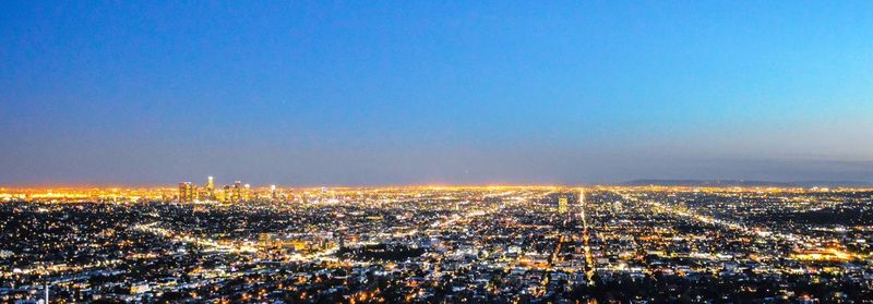 Aerial view of illuminated cityscape against clear blue sky