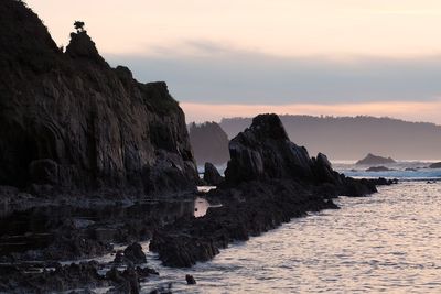 Rock formations by sea against sky during sunset