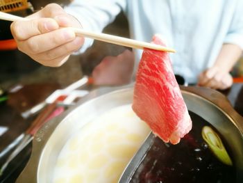 Midsection of chef holding beef slice with chopsticks over utensil in kitchen