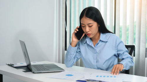 Young woman using phone while sitting on table