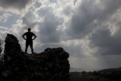 Silhouette man standing on rock against sky