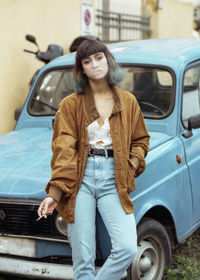 Portrait of woman smoking cigarette while leaning on car