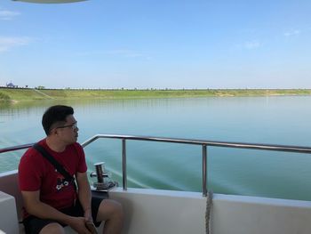 Man sitting on railing by lake against sky