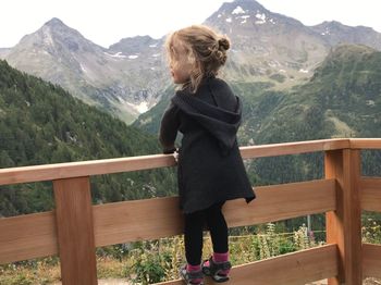 Girl standing on railing against mountains