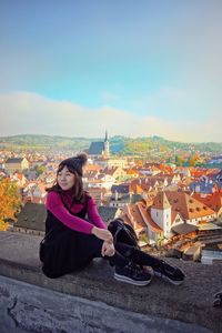 Woman sitting on retaining wall against cityscape