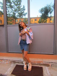 Full length portrait of smiling woman standing against window