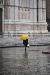 Full length of woman walking with yellow umbrella on wet street in city during rainy season