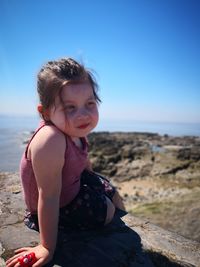 Smiling cute girl sitting on rock against sea at beach