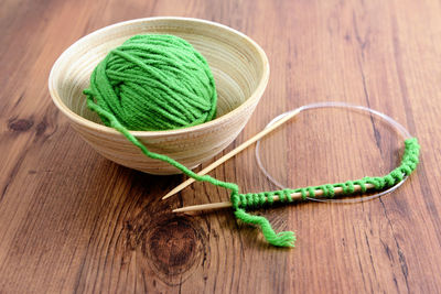 Knitting needles with ball of green wool on table