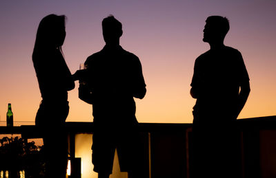 Silhouette people standing against orange sky