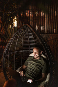 Smiling man using laptop while sitting in hanging chair at night