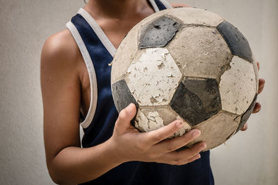 Midsection of boy standing with soccer ball against wall