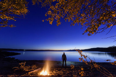 Man standing by lake against blue sky