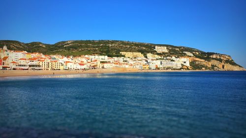 Scenic view of sea by city against clear blue sky