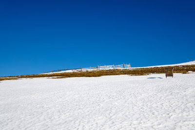 Snow covered land against clear blue sky