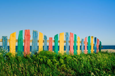 Multi colored railing on grassy sea shore against clear blue sky