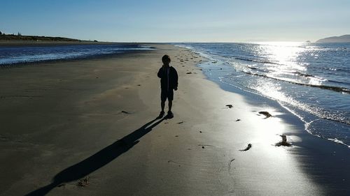 Full length of boy standing on sea shore at beach against clear sky during sunny day