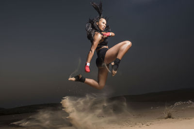 Young woman jumping on sand against sky