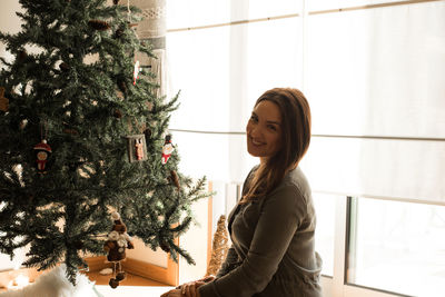 Portrait of smiling woman sitting by christmas tree at home