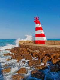 Lighthouse on rocks by sea against sky