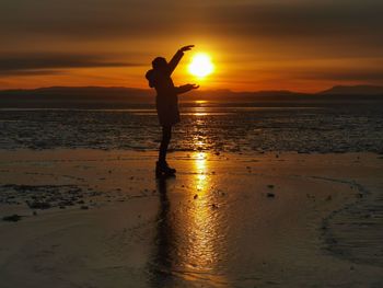 Silhouette man standing on beach against sky during sunset