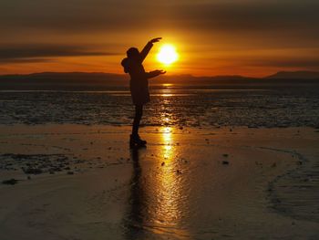 Silhouette man standing on beach against sky during sunset