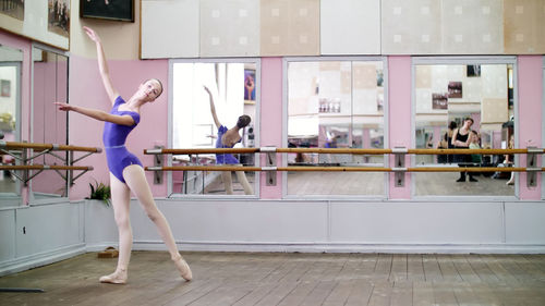 In dancing hall, young ballerina in purple leotard performs tour chenne on pointe shoes