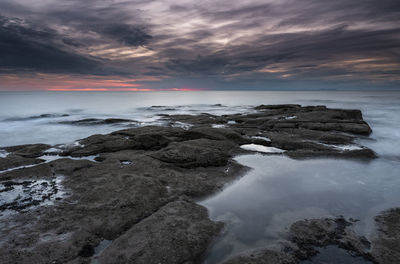 Rocks by sea against sky during sunset