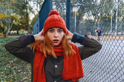 Bright cute young woman in orange warm knitted hat and scarf hands near head. emotion of concern.